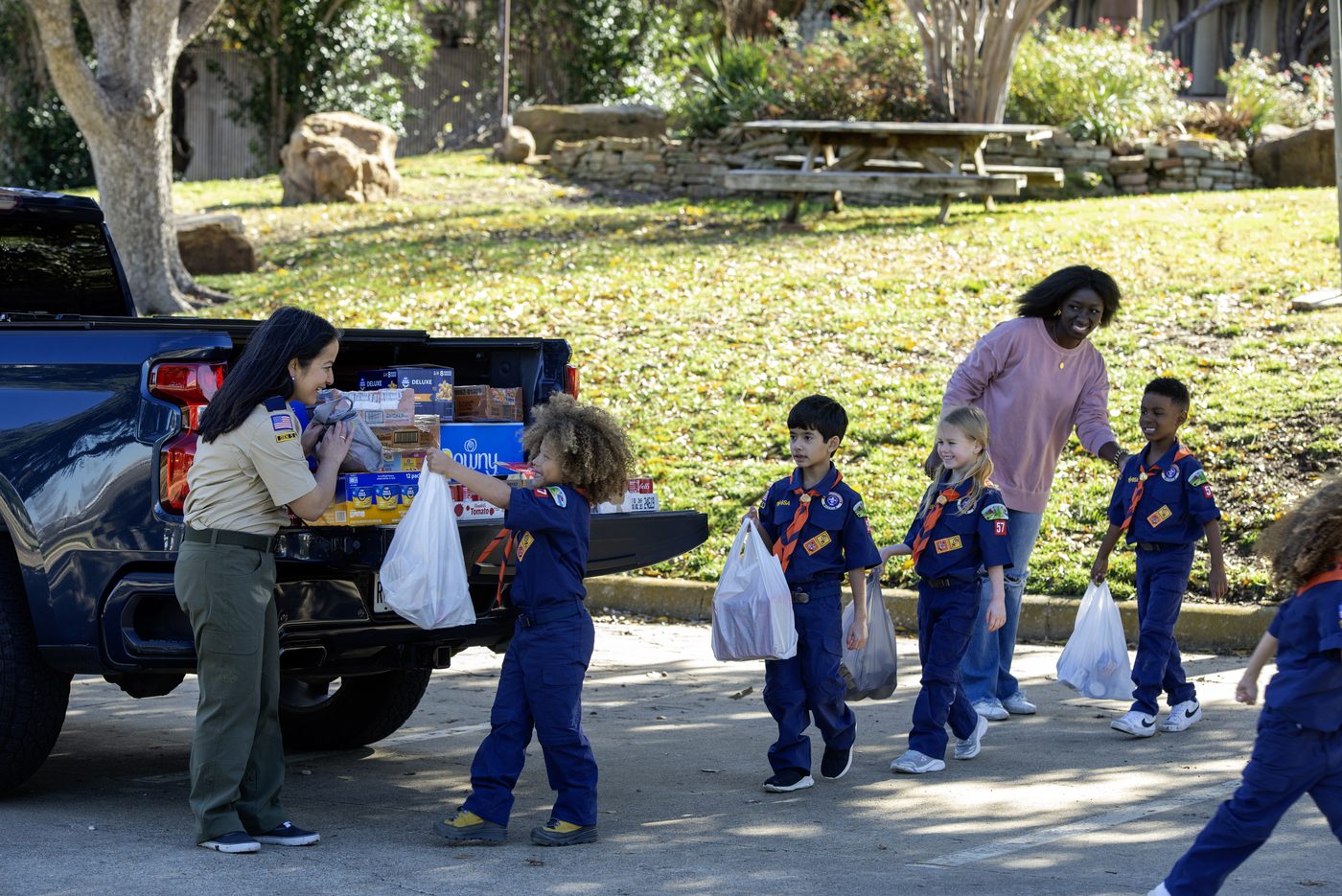 Cub Scouts carrying bags of donated food to a pickup truck during a collection drive.