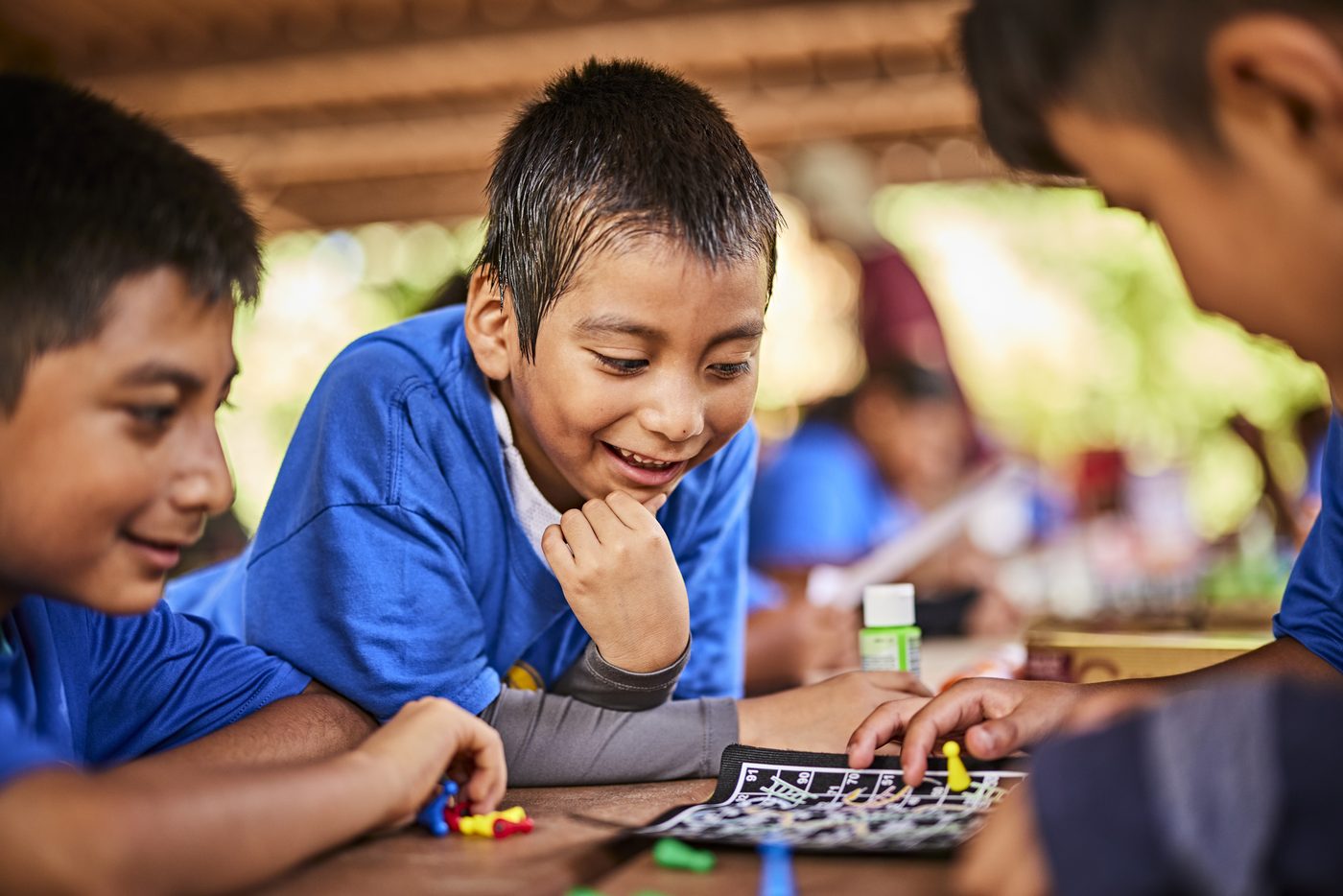 Cub Scouts leaning over a board game together at a table, grinning.